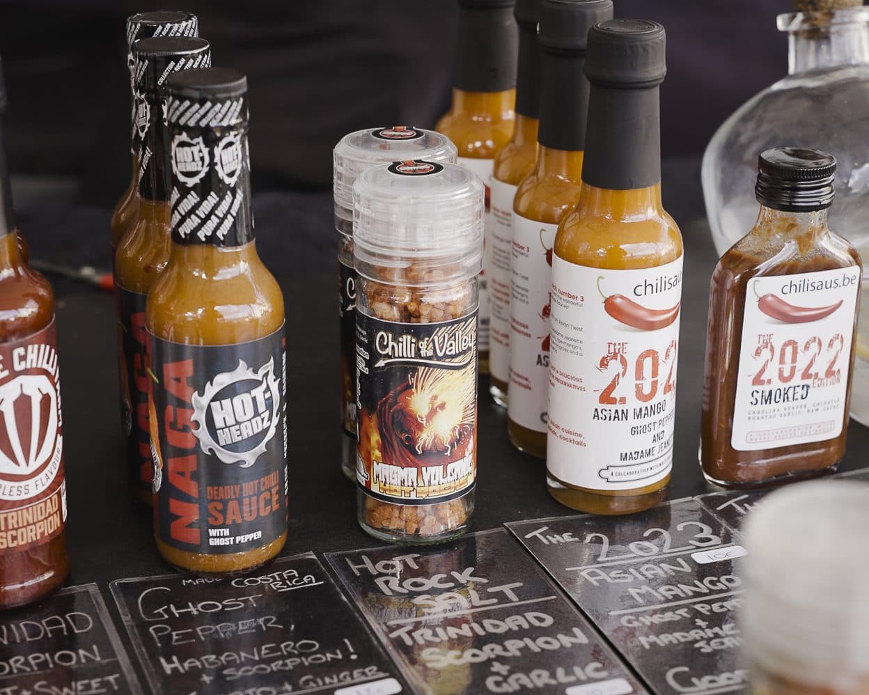 A line-up of hot sauce bottles with handwritten chalkboard tasting notes at Berlin Chili Fest.